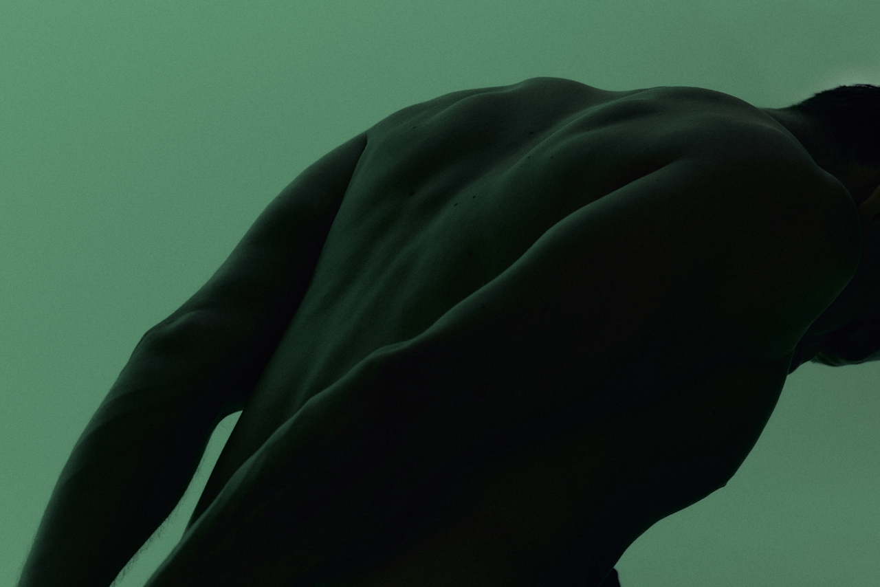 Close-cropped image of a muscular back silhouette against a deep green background