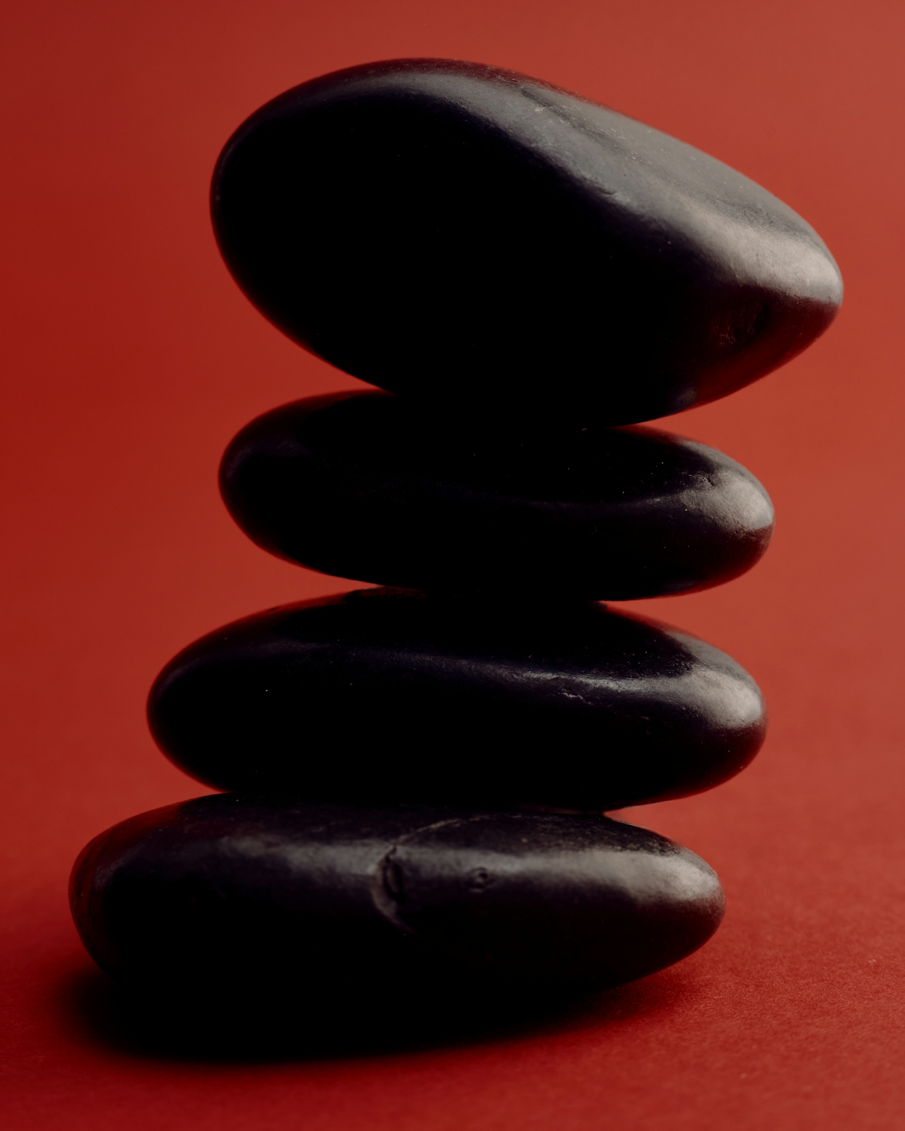 A stack of four smooth black stones on a rich red background