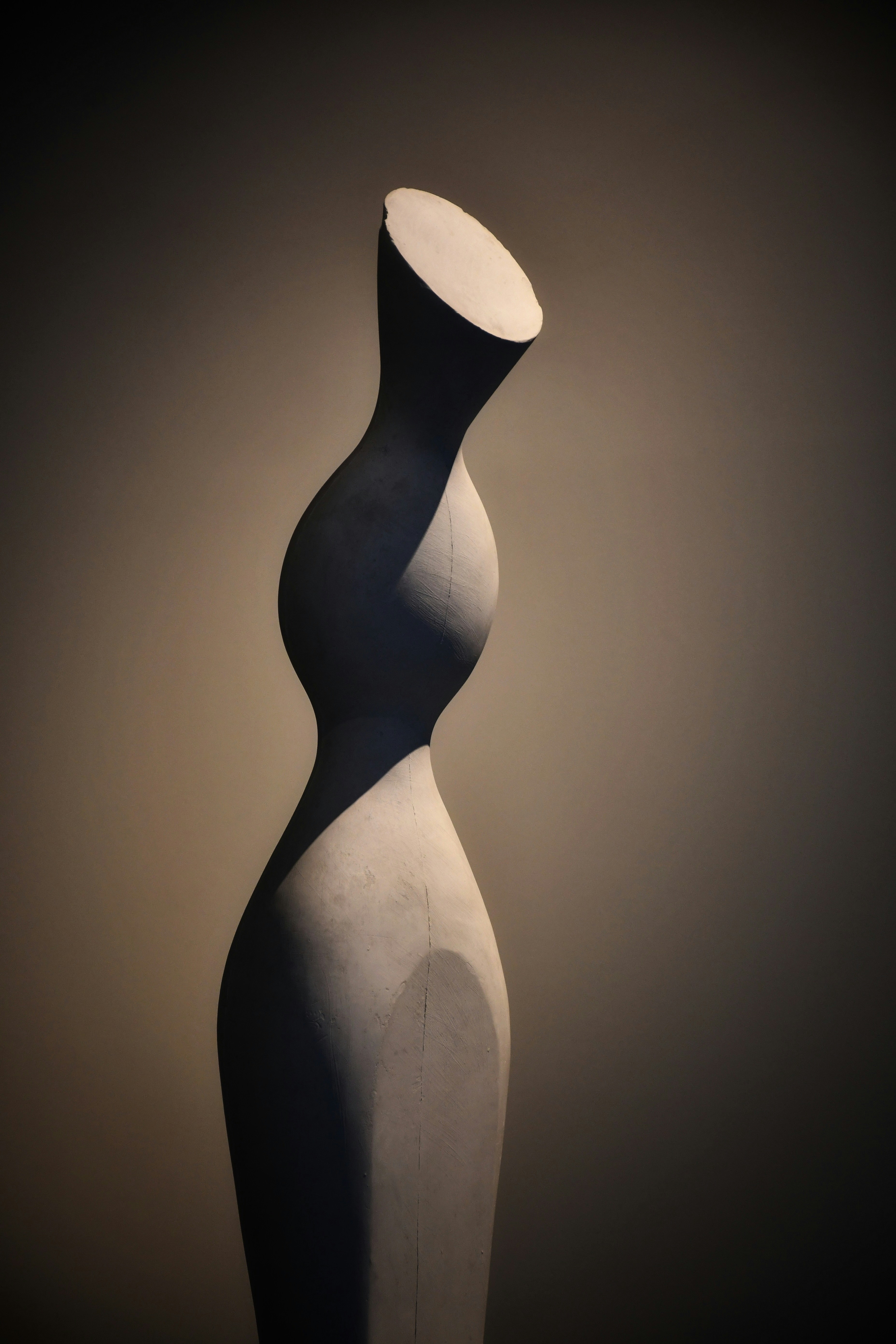 A ceramic sculpture photographed with dramatic dark lighting on a rich brown background